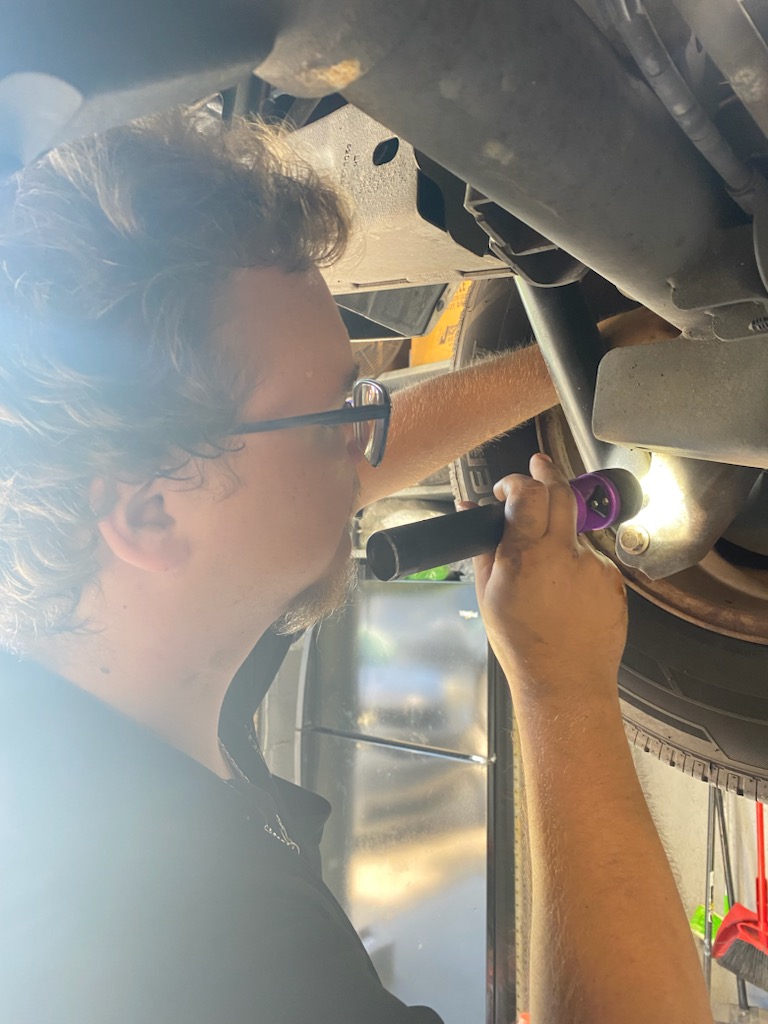 Holiday Car Inspection Tips | Griffis Automotive Repair | Orlando, FL. Image of Griffis Automotive Repair mechanic holding a flashlight to inspect inside tire on car that is lifted in shop.