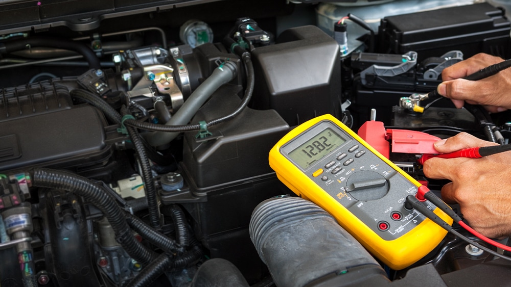 6 signs your car battery needs to be replaced in Orlando, FL with Griffis Automotive Repair. Image of mechanic hands using battery testing equipment to test a car battery in shop.